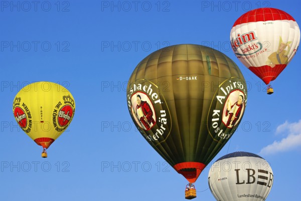 Four hot air balloons with lots of colourful advertising rise into the air with passengers on