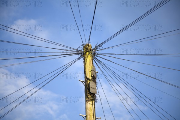 Telephone line cables radiating out fro telegraph pole against blue sky, UK