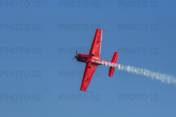Red stunt aerobatic plane performing stunts in blue sky. Concept of speed, difficulty, precision,