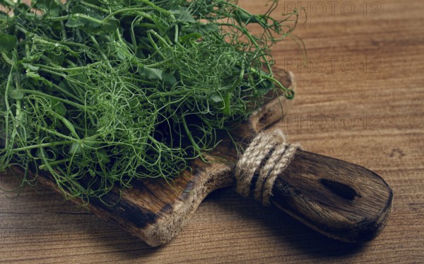 A rustic wooden cutting board holds a pile of fresh microgreens, showcasing vibrant colors and