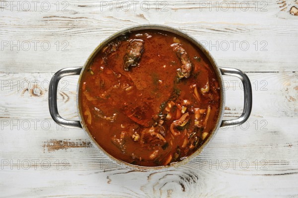 Overhead view of a silver pot with two handles on a white wooden table. The pot is filled with a
