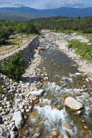 Wilder Fluss, der durch eine steinige Berglandschaft fließt, mit grünen Bäumen und Hügeln unter