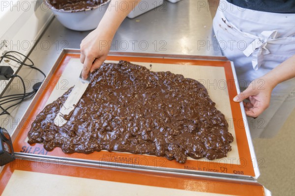 A person spreads and smoothes chocolate with a spatula on a baking mat, Burch Schokolade