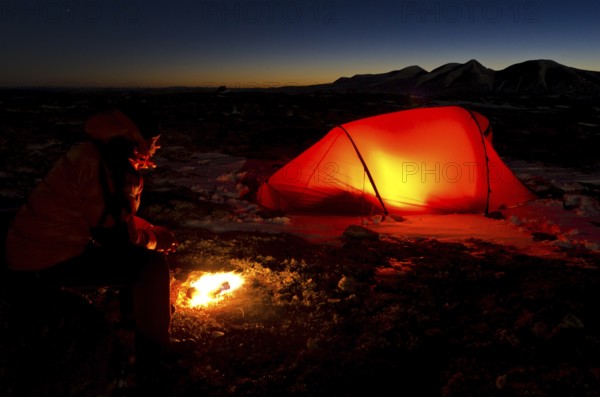 Man with campfire and lit tent, Engerdalsfjellet, Rendalssölen peak in the background, Hedmark