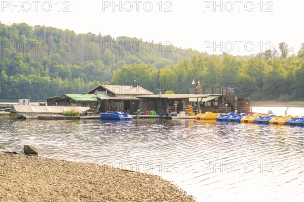 A lake with a jetty for boats and surrounded by huts and forest, Rappbodetalsperre, Harz, Germany,
