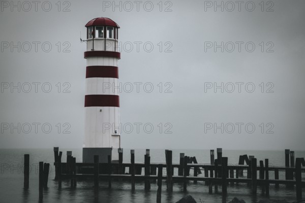 A red and white lighthouse stands on the lake on a foggy day, Podersdorf, Burgenland, Austria,
