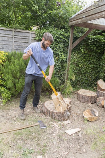 Young man using log splitter tool to split pine tree logs, Suffolk, England, UK