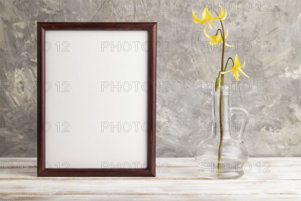 Wooden frame with yellow trout lily or dogtooth violet flowers in glass on gray concrete background