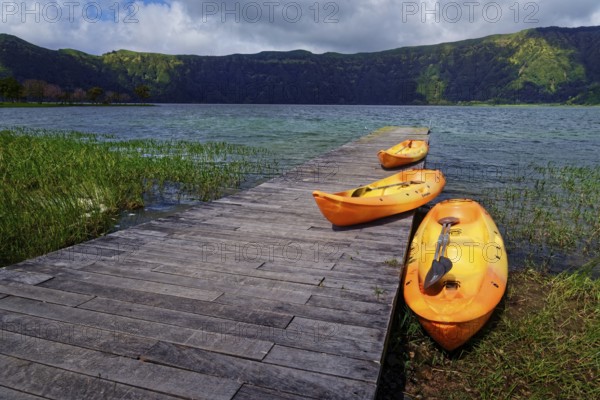 Three orange kayaks on the wooden jetty of the crater lake Lagoa Azul, surrounded by greenery and