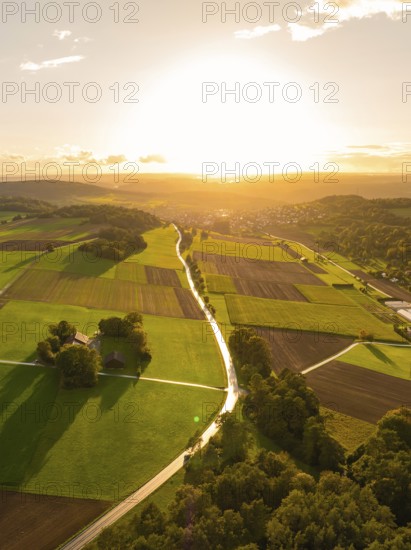 Extensive fields and trees in the glowing red light of the sunset with reflecting sunlight,