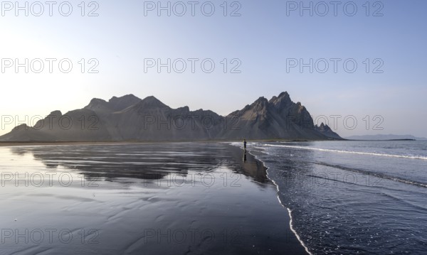 Tourist at black lava beach, sandy beach and sea, mountains Klifatindur reflected in the water,