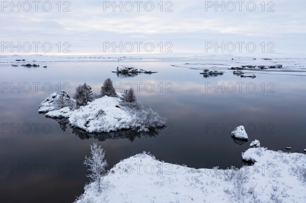 Snow-covered small islands overgrown with bushes in Lake Myvatn, at blue hour, Kalfaströnd, drone