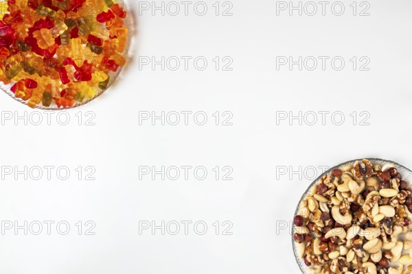 Comparison of unhealthy and healthy, gummy bears and various nuts, on plates, white background,