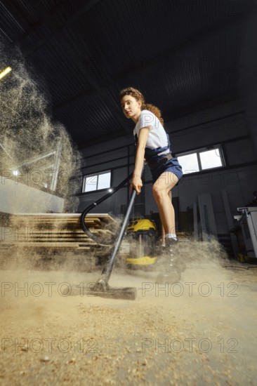 Young woman using vacuum cleaner in a carpentry workshop at the end of a work shift