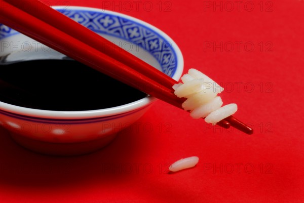 Rice grains on chopsticks, bowl with soy sauce, chopsticks, rice