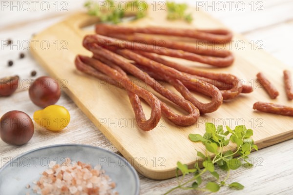 Traditional polish smoked pork sausage kabanos on cutting board with salt and pepper on white