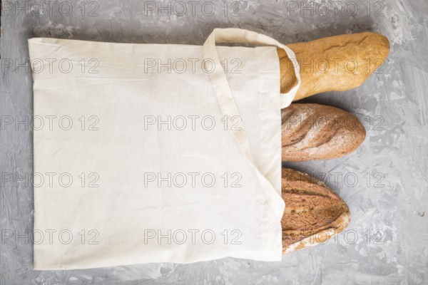 Reusable textile grocery bag with fresh baked bread on a gray concrete background. top view, flat