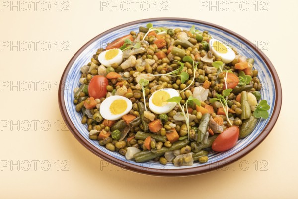 Mung bean porridge with quail eggs, tomatoes and microgreen sprouts on a pastel orange background.