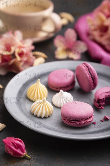 Purple macarons or macaroons cakes with cup of coffee on a black concrete background and pink