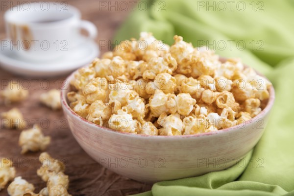 Popcorn with caramel in ceramic bowl on brown concrete background and green textile. Side view,