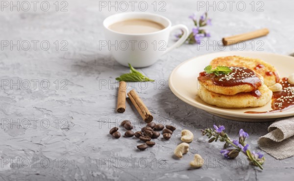 Cheese pancakes with caramel sauce on a beige ceramic plate and a cup of coffee on a gray concrete