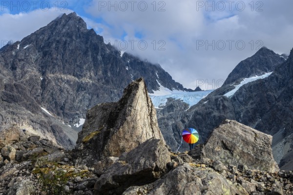 Woman with colorful open umbrella between large rocks, glacier Lenangsbreen, at glacier lake