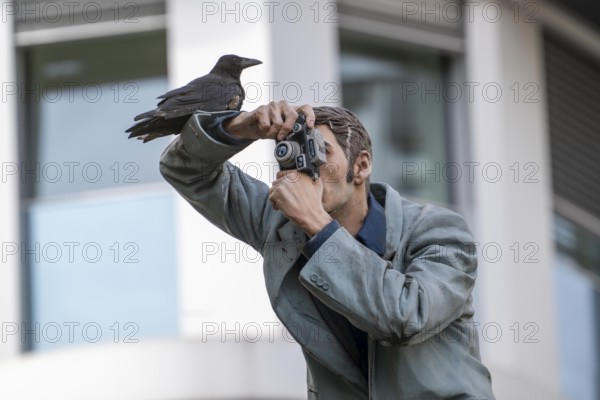 Real crow on a pillar saint, The Photographer, in front of the main railway station in Düsseldorf,