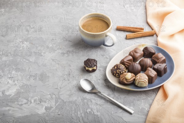 Different chocolate candies and a cup of coffee on a gray concrete background and orange textile.