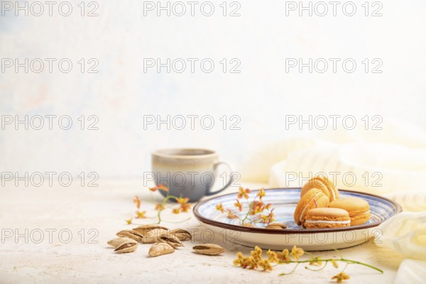 Orange macarons or macaroons cakes with cup of coffee on a white concrete background and linen