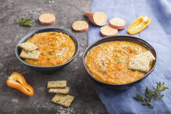 Sweet potato or batata cream soup with sesame seeds and snacks in blue ceramic bowls on a black