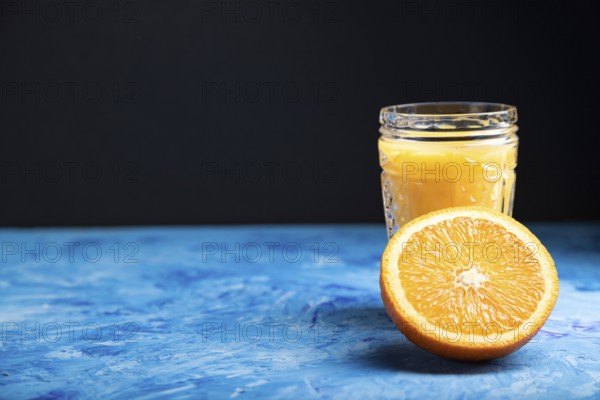 Glass of orange juice on a black and blue background. Hard light, contrast. Side view, copy space