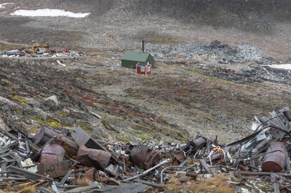 Cabin near scrap yard in rocky, hilly landscape with snow remains, arctic settlement