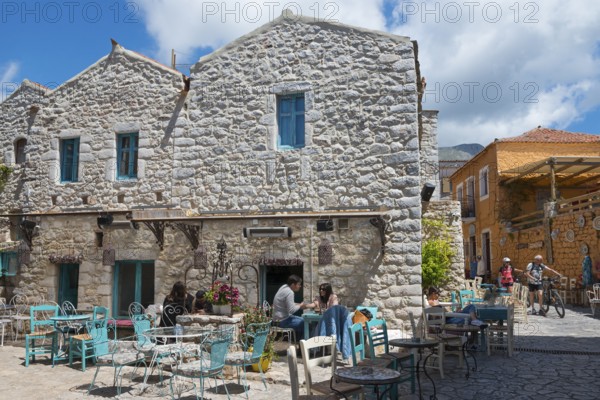 People relaxing in a terrace café in front of a traditional stone house with blue shutters, Old