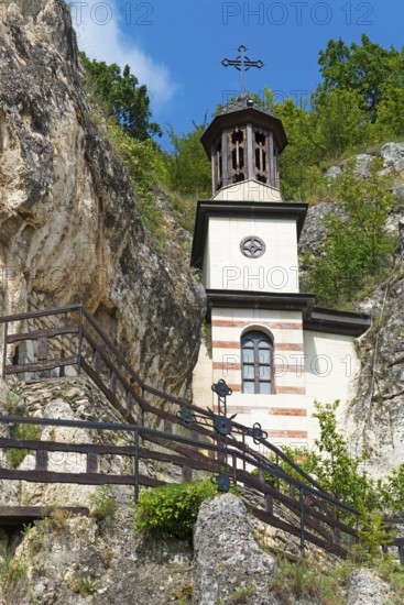 Bell tower with clock and cross surrounded by stairs and blue sky, Bulgarian Orthodox cave