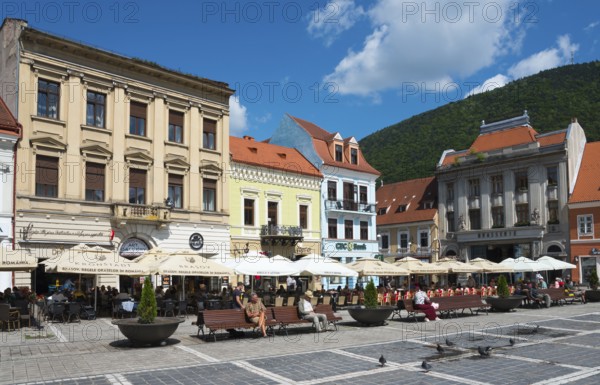 People sitting in outdoor cafés in front of historical buildings on a sunny day in a city, town