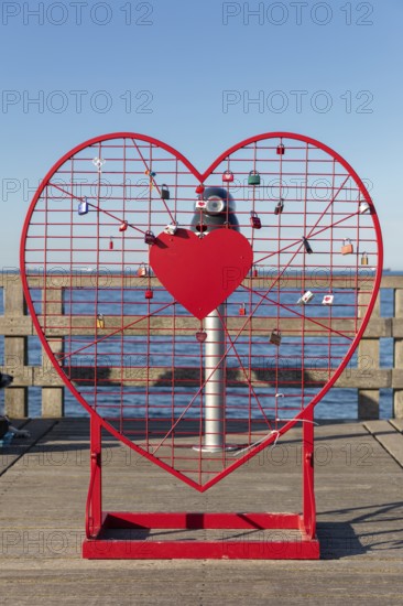 A red heart with padlocks stands on the pier in front of the blue sea horizon, Rügen, Binz