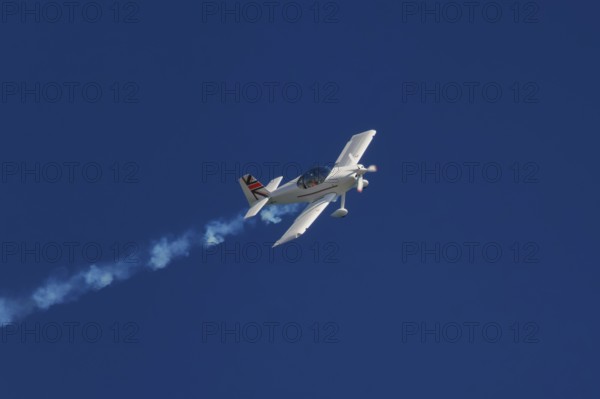 Stunt aerobatic plane performing stunts in blue sky with smoke trail. Concept of speed, difficulty,