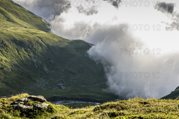 Dramatic mountain landscape with low-hanging clouds and green valleys, alpine hut, Neukirchen am