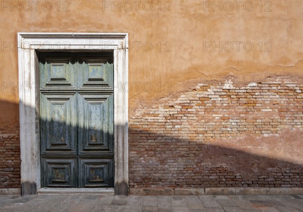 Red house facade with large green door, peeling plaster on brick wall, Venice, Veneto, Italy,
