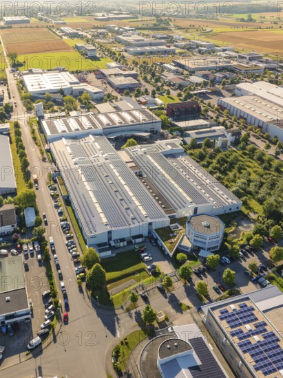An industrial area with several buildings, roads and solar modules, surrounded by fields, taken