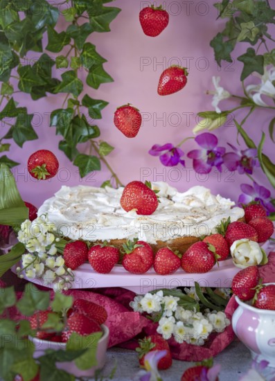 Strawberry cake with meringue decorated with strawberries and flowers against a pink background