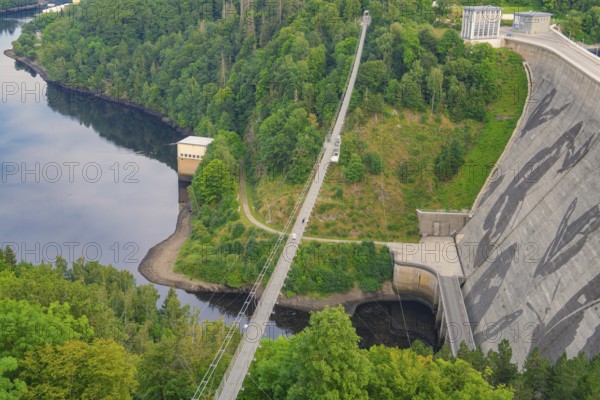 View of a bridge crossing a dam surrounded by dense forest and a calm body of water,