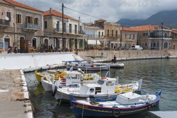 Small harbour with fishing boats in front of a row of traditional stone buildings on the coast with