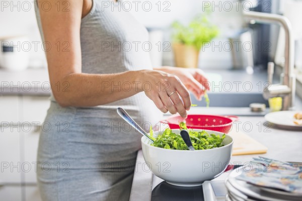 A pregnant woman washes and prepares fresh salad in the kitchen