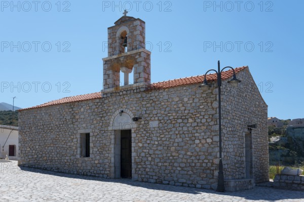 Historic stone church with bell tower and red roof under a blue sky in a Mediterranean setting,