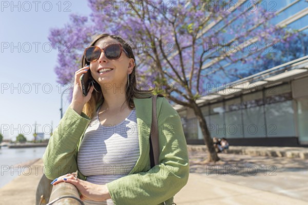 Businesswoman using smartphone near blooming jacaranda mimosifolia tree, enjoying sunny day in