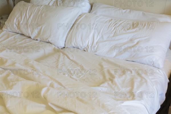 Close-up of rippled and creased white cotton bed sheets and pillows on unmade king size bed, La