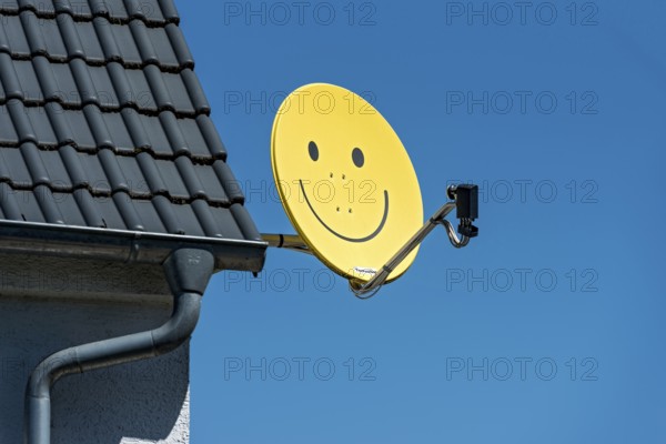 Funny satellite dish, yellow with smiley, satellite antenna on the roof of a house, satellite