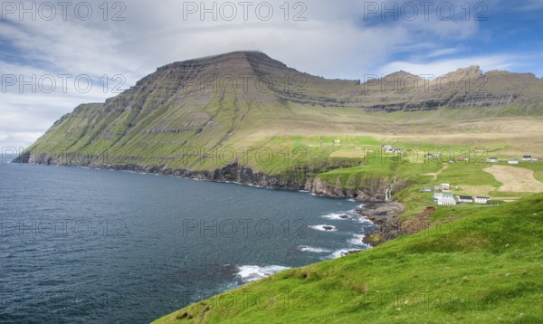 Green coastal landscape with mountains and houses under a blue sky, Vidareidi, Vidoy Island,