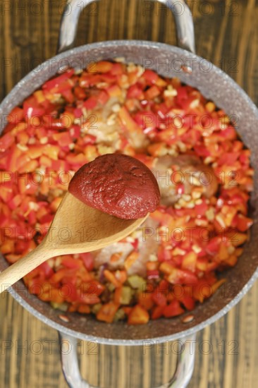 Adding a tomato paste to a pot with chopped red and green bell peppers, onions, and seasonings